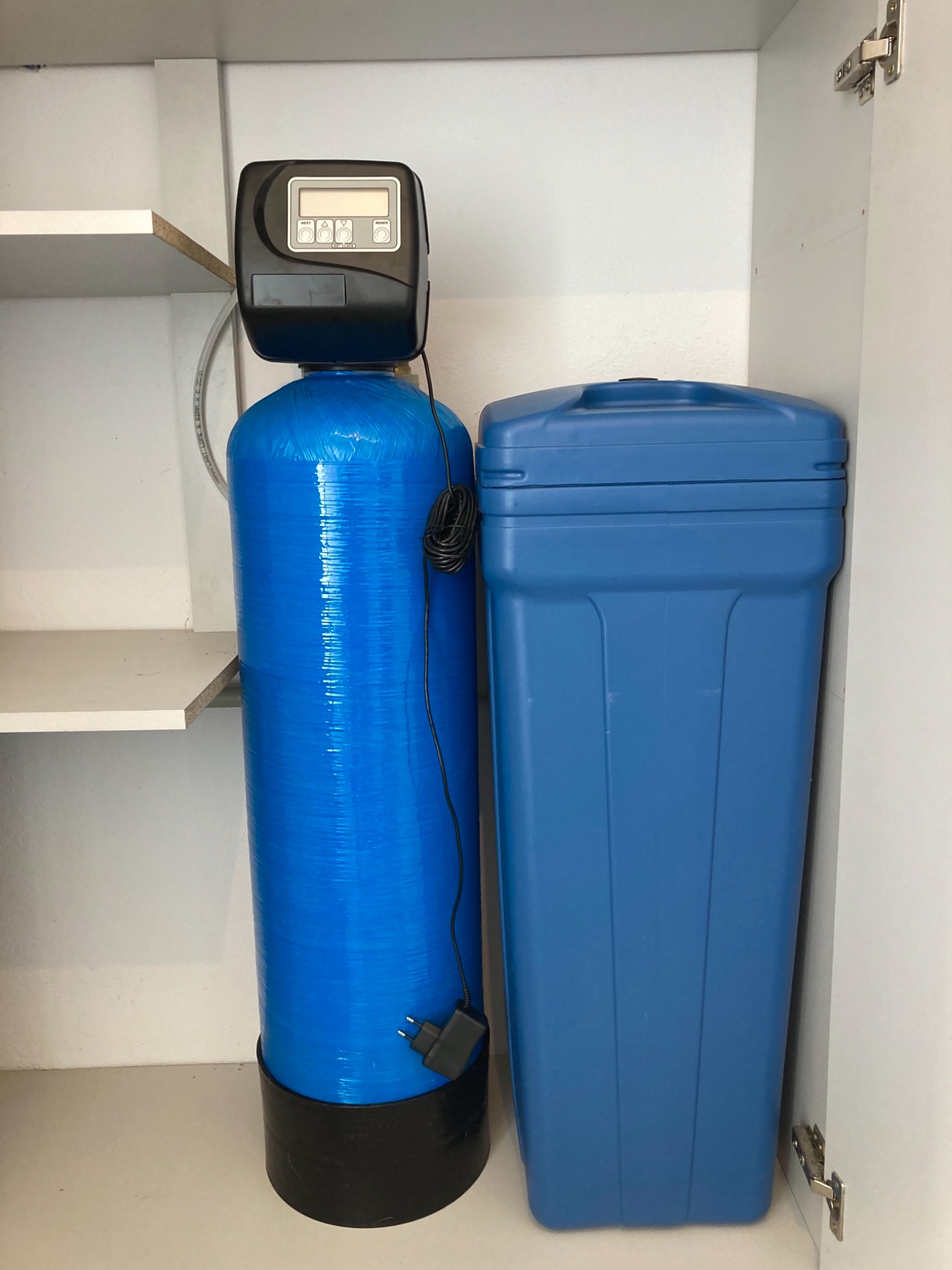 Niebieski zbiornik na wodę z czarnym panelem sterowania i niebieski pojemnik na sól w białej szafce.
