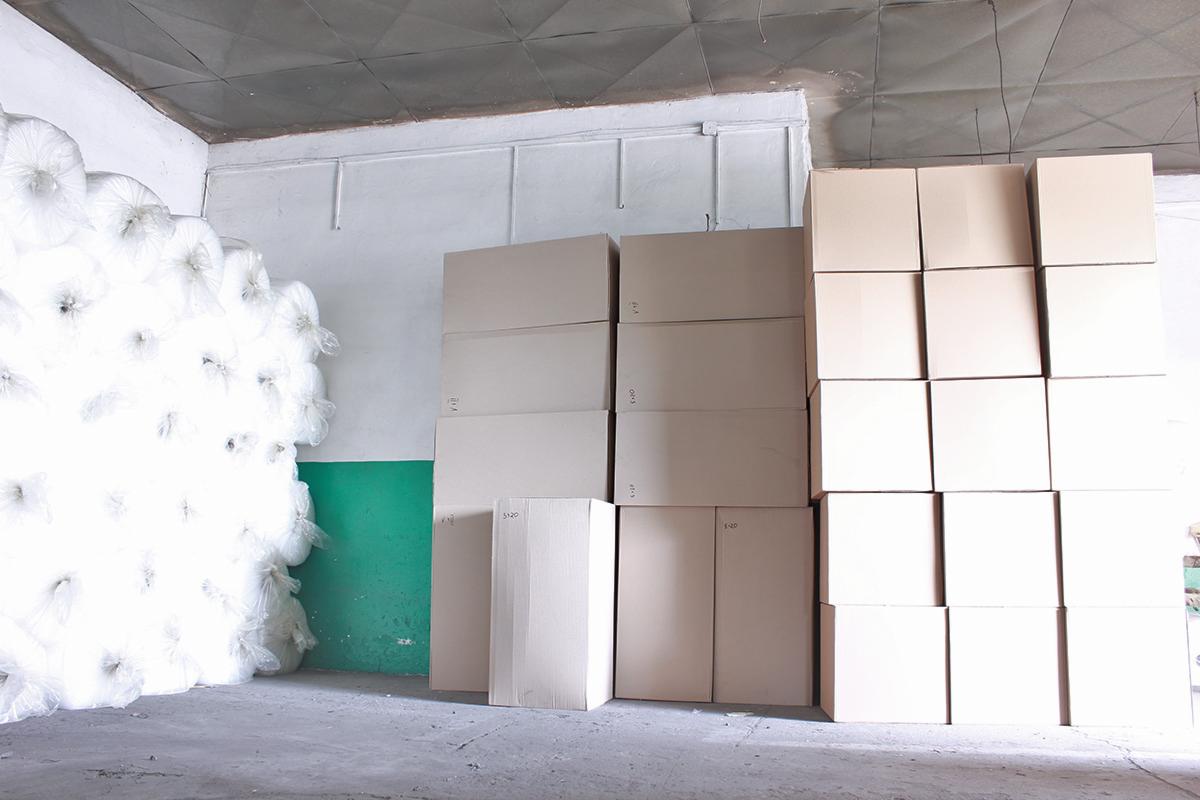 Stos kartonowych pudeł i sterta folii bąbelkowej w magazynie, na ścianie widoczny zielony pas.