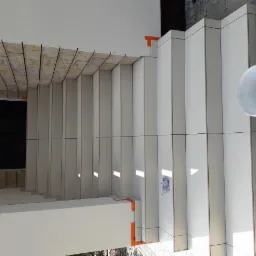 Wykończone schody zewnętrzne z białych płytek, widoczny fragment elewacji z kamienia dekoracyjnego i wiadro po farbie na kostce brukowej obok schodów.