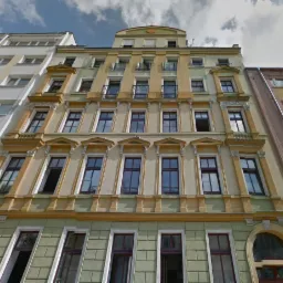 Fasada kamienicy z elementami dekoracyjnymi, widok z dołu na budynek z oknami i balkonami.