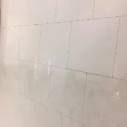 Błyszcząca, jasna podłoga z płytek po umyciu, widoczne zacieki i mokre plamy, w tle kartony z boku ściany.