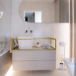 Nowoczesna łazienka w Rzeszowie z białą, prostokątną umywalką na szafce z szufladami, złotą ramą i dekoracyjnymi akcesoriami, oświetlona od dołu.