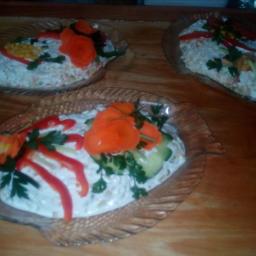 catering - Trzy porcje sałatki jarzynowej ułożone w szklanych miseczkach w kształcie ryb, udekorowane różyczkami z marchewki, paskami czerwonej papryki i natką pietruszki na drewnianym stole.