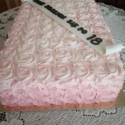 catering - Kwadratowy tort urodzinowy pokryty kremem w kształcie róż w odcieniach różu i bieli, z dekoracyjnym napisem 'Sto lat szczęścia po 18' na białej wstędze.