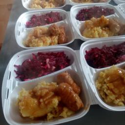 catering - Porcje obiadowe w styropianowych pojemnikach: puree ziemniaczane z sosem, buraczki i dwie parówki, przygotowane do transportu.