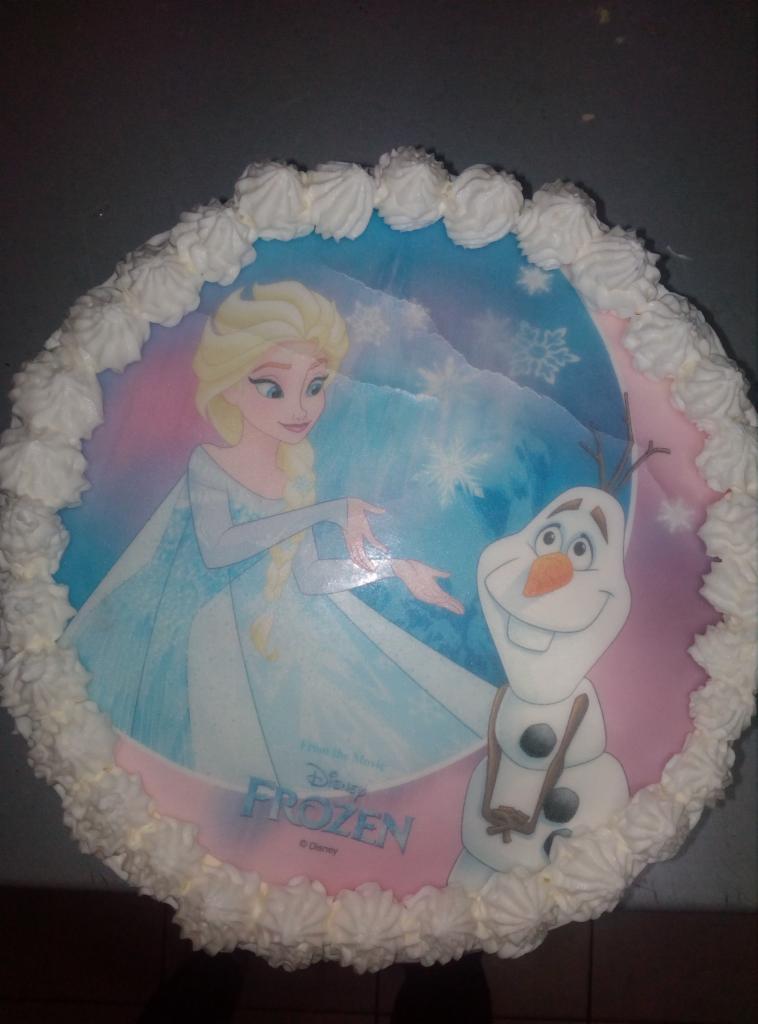 Okrągły tort z kremem, dekorowany jadalnym nadrukiem z postaciami z filmu animowanego 'Frozen', przedstawiający Elsę i Olafa na tle śnieżynek.