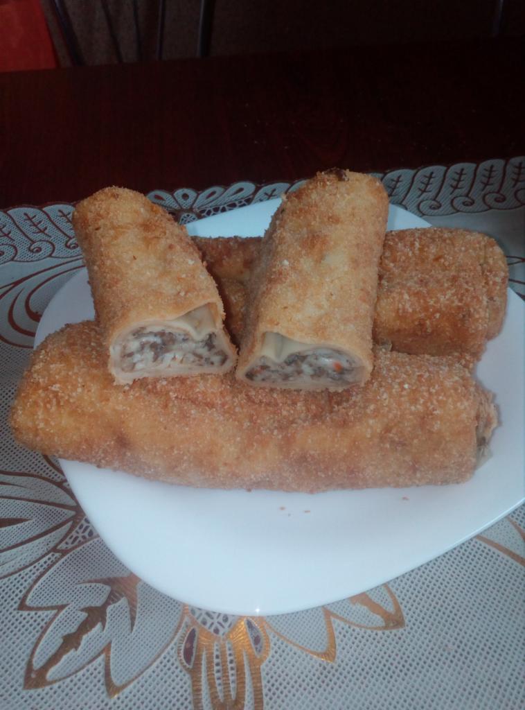 Krokiety z mięsem i kapustą na białym talerzu, dwa przekrojone, ukazujące farsz, na obrusie w kwiaty.