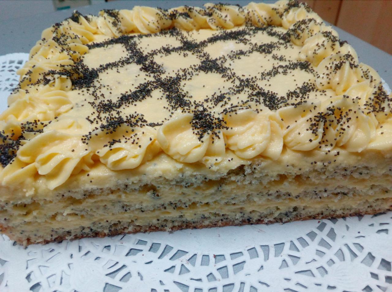 Kwadratowy tort makowy z kremem waniliowym, dekorowany rozetkami z kremu i posypką z maku, ułożony na białej serwetce.