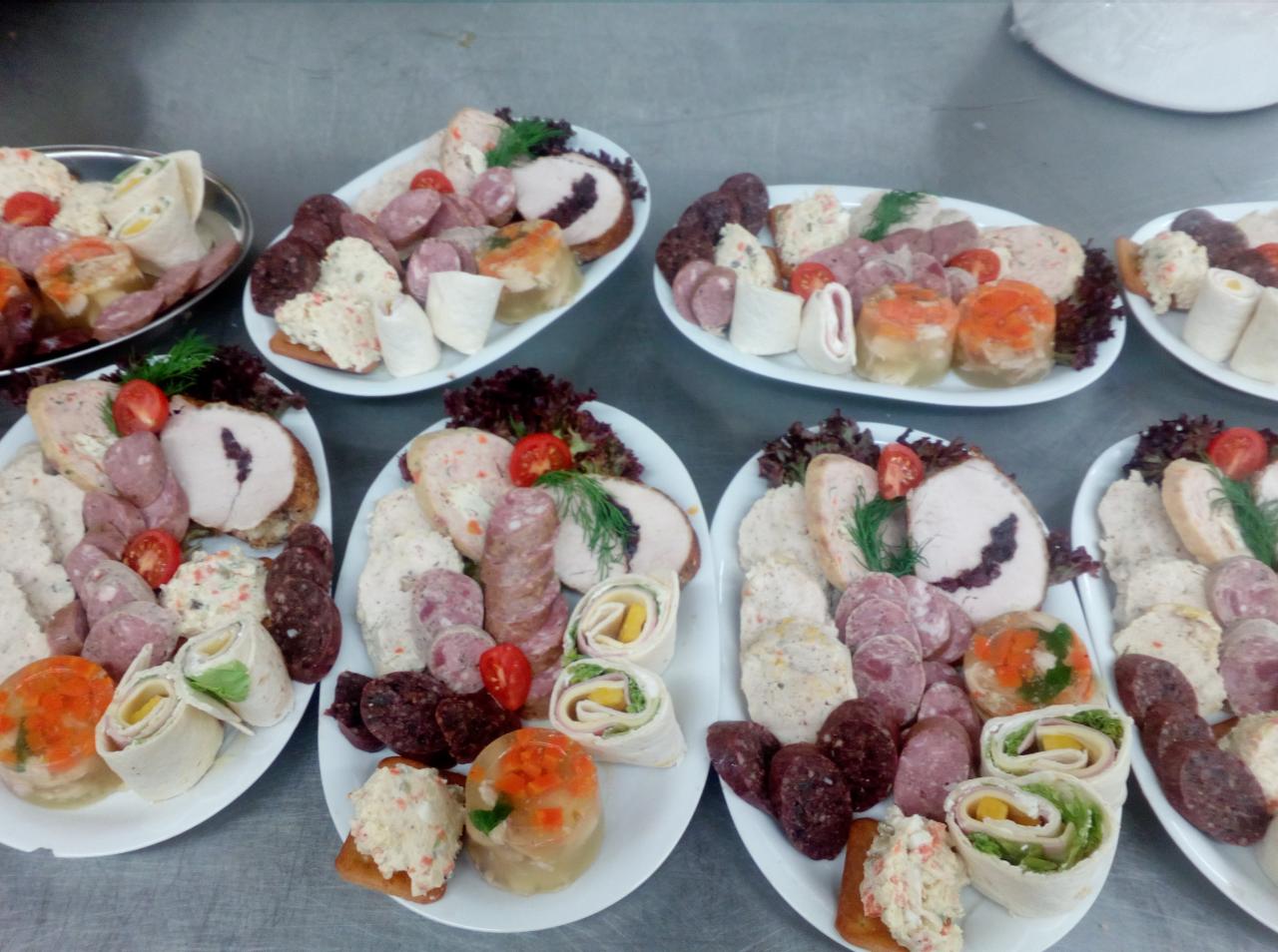 Dekoracyjnie ułożone na talerzach wędliny, pasztety, galaretki i roladki, z dodatkiem sałaty i pomidorów koktajlowych, przygotowane do serwowania.