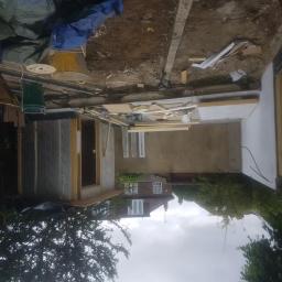 Raman construction fcb - Budowa małego pomieszczenia z izolacją zewnętrzną, widoczne materiały budowlane i narzędzia, w tle dom jednorodzinny.