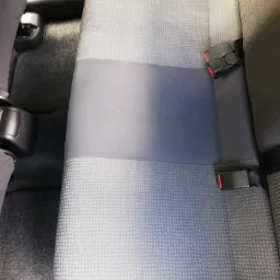 Wnętrze samochodu z widoczną tylną kanapą z szarej tapicerki z wzorem w kropki i czarnymi pasami bezpieczeństwa.