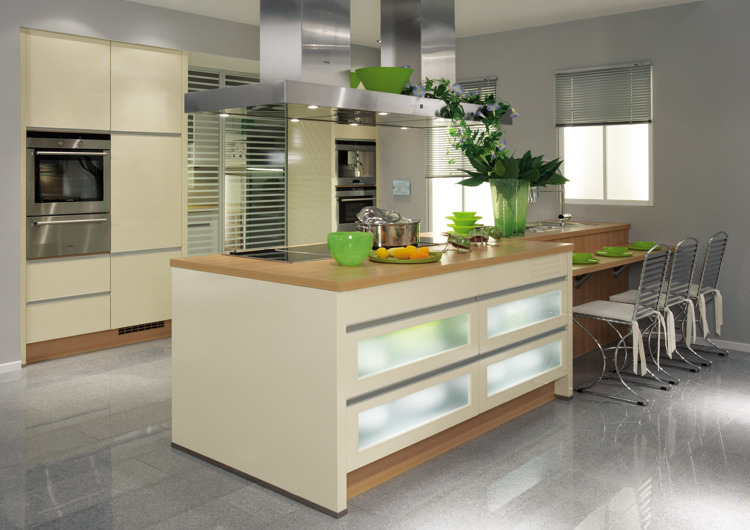 Jasna, nowoczesna kuchnia z wyspą i frontami szafek z mlecznego szkła, stalowym okapem i blatem z drewna, uzupełniona zielonymi akcentami dekoracyjnymi.