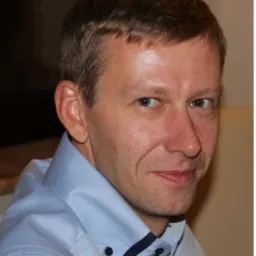 Portret mężczyzny w błękitnej koszuli, skierowany lekko w prawo, z widocznymi zmarszczkami mimicznymi wokół oczu.