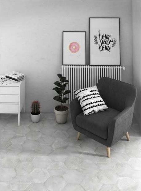 Salon z szarymi, heksagonalnymi płytkami podłogowymi, szarym fotelem z drewnianymi nogami i poduszką w czarno-białe wzory, grzejnikiem, komodą, kaktusem i dwoma plakatami na ścianie.
