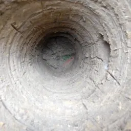 Wnętrze wywierconego otworu w ziemi z widocznymi śladami wiertła, niewielkimi fragmentami roślin i pomarańczowym znacznikiem na dnie.