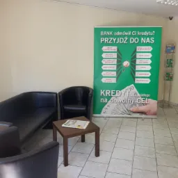 Poczekalnia z sofami i stolikiem z gazetą, w tle baner reklamowy z hasłem: Bank odmówił Ci kredytu? Przyjdź do nas, oraz informacjami o korzyściach oferty.