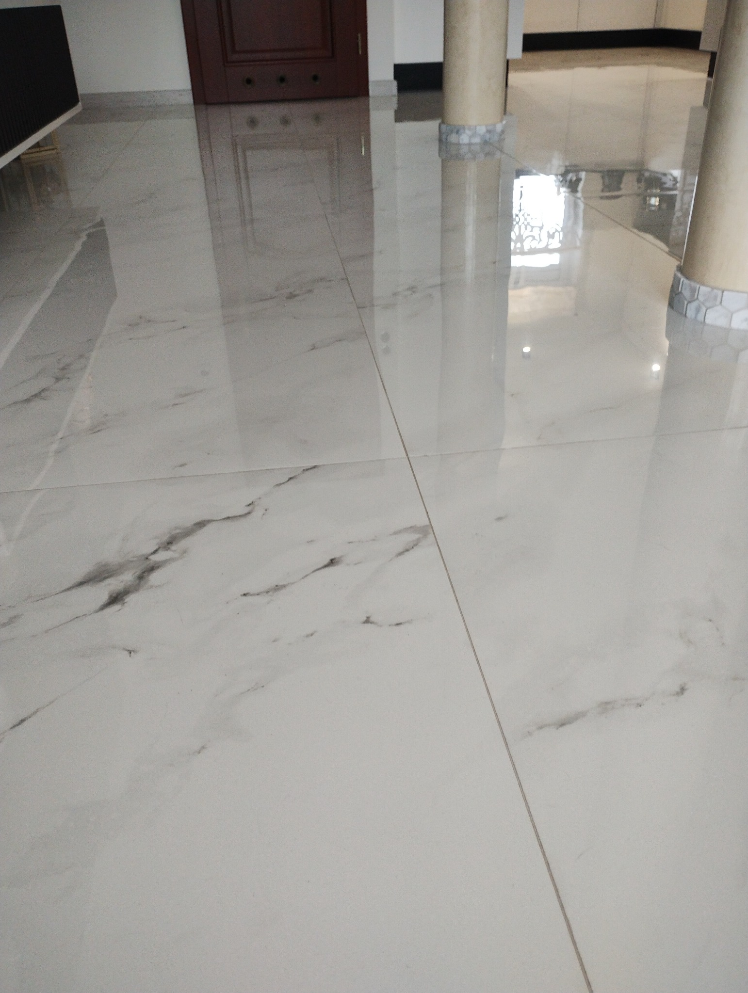 Błyszcząca, biała podłoga z marmurowym wzorem, ułożona z płytek, widoczne kolumny i drzwi w tle.