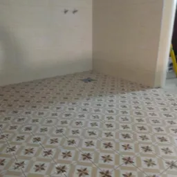 Wykończona łazienka z beżowymi płytkami podłogowymi w kwiaty i jasnymi płytkami ściennymi, widoczne dwa uchwyty na ścianie i odpływ podłogowy.