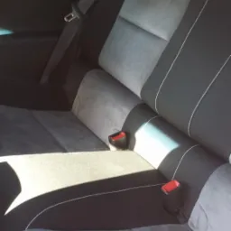 Tylne siedzenie samochodu po renowacji, tapicerowane szarą i czarną tkaniną z białymi szwami, widoczne pasy bezpieczeństwa i pluszowe kostki do gry w tle.