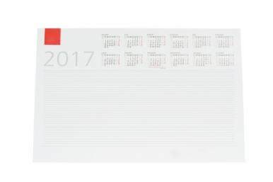 Biały kalendarz biurkowy na rok 2017 z czerwonym znacznikiem i liniami do notatek pod mini-kalendarzami miesięcznymi.