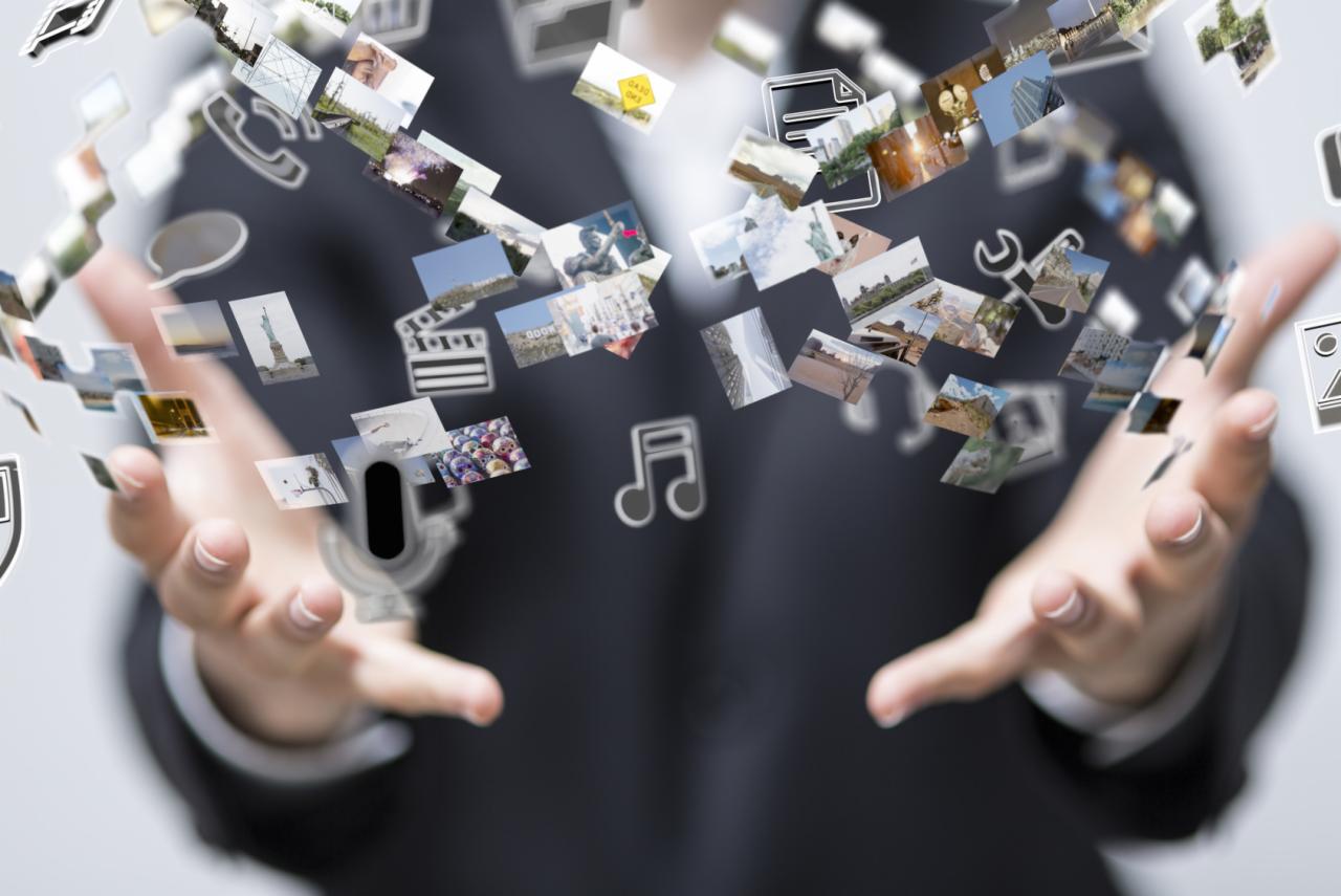 Dłonie mężczyzny w garniturze, unoszące w przestrzeni miniaturowe zdjęcia i ikony, tworząc wizualizację cyfrowych treści i multimediów.