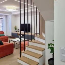 Nowoczesne wnętrze domu z otwartą przestrzenią: salon z pomarańczową sofą i schodami z drewnianymi stopniami i czarnymi balustradami, widok z dołu na górę.