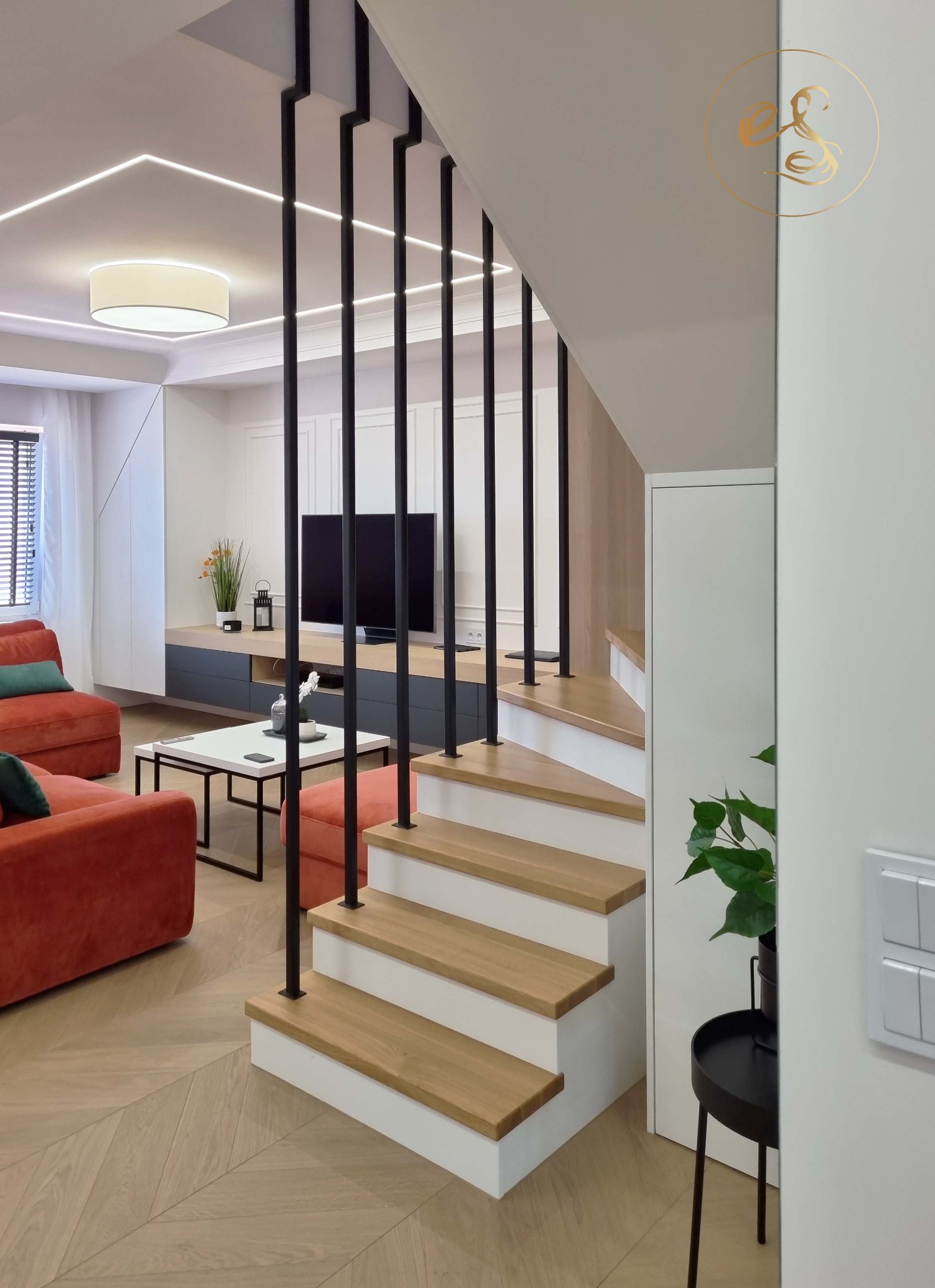 Nowoczesne wnętrze domu z otwartą przestrzenią: salon z pomarańczową sofą i schodami z drewnianymi stopniami i czarnymi balustradami, widok z dołu na górę.