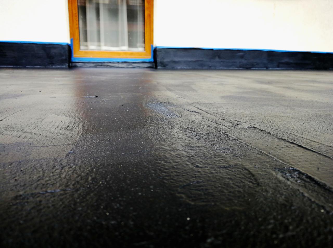 Świeżo zaizolowany fundament budynku z widocznym oknem zabezpieczonym niebieską taśmą malarską.