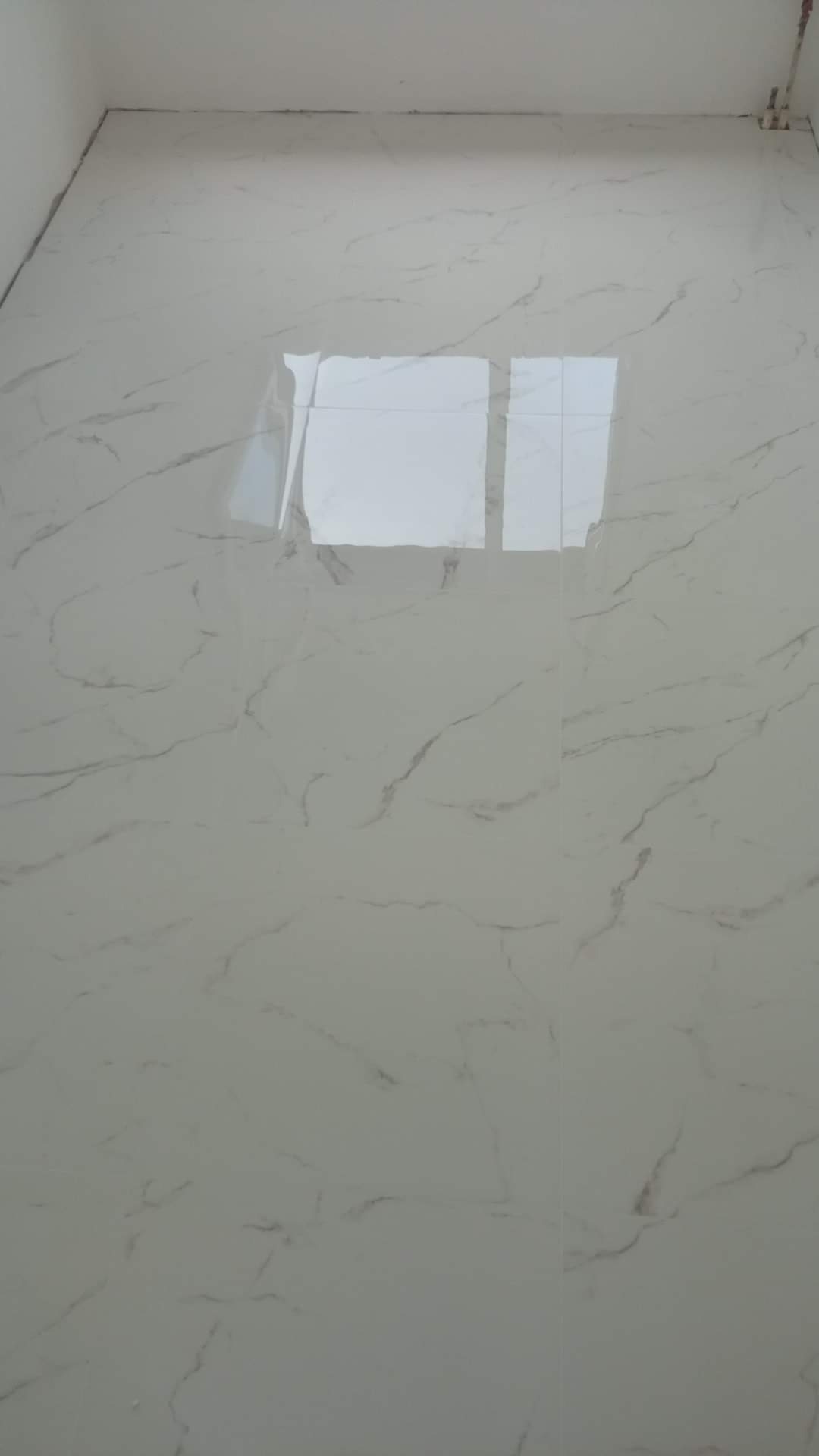 Błyszcząca podłoga wyłożona jasnymi płytkami imitującymi marmur, z widocznymi refleksami światła odbijającymi się od gładkiej powierzchni.