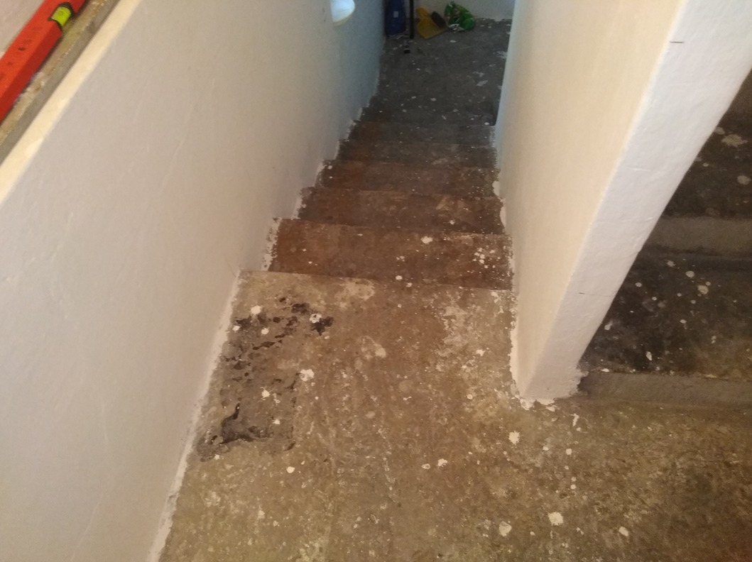 Schody w trakcie remontu, ściany świeżo pomalowane na biało, podłoga i schody z widocznymi plamami farby i resztkami zaprawy.