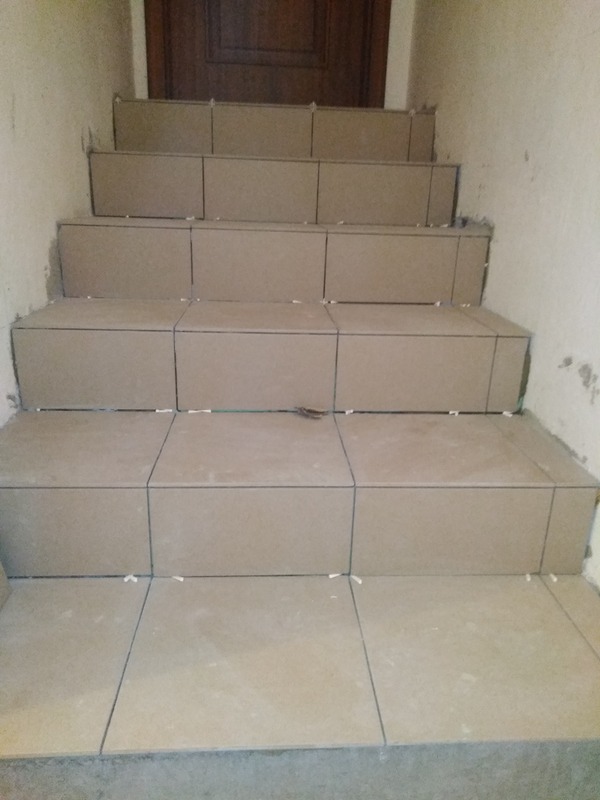 Schody w trakcie układania płytek ceramicznych, widoczne krzyżyki dystansowe i niezagruntowane ściany.