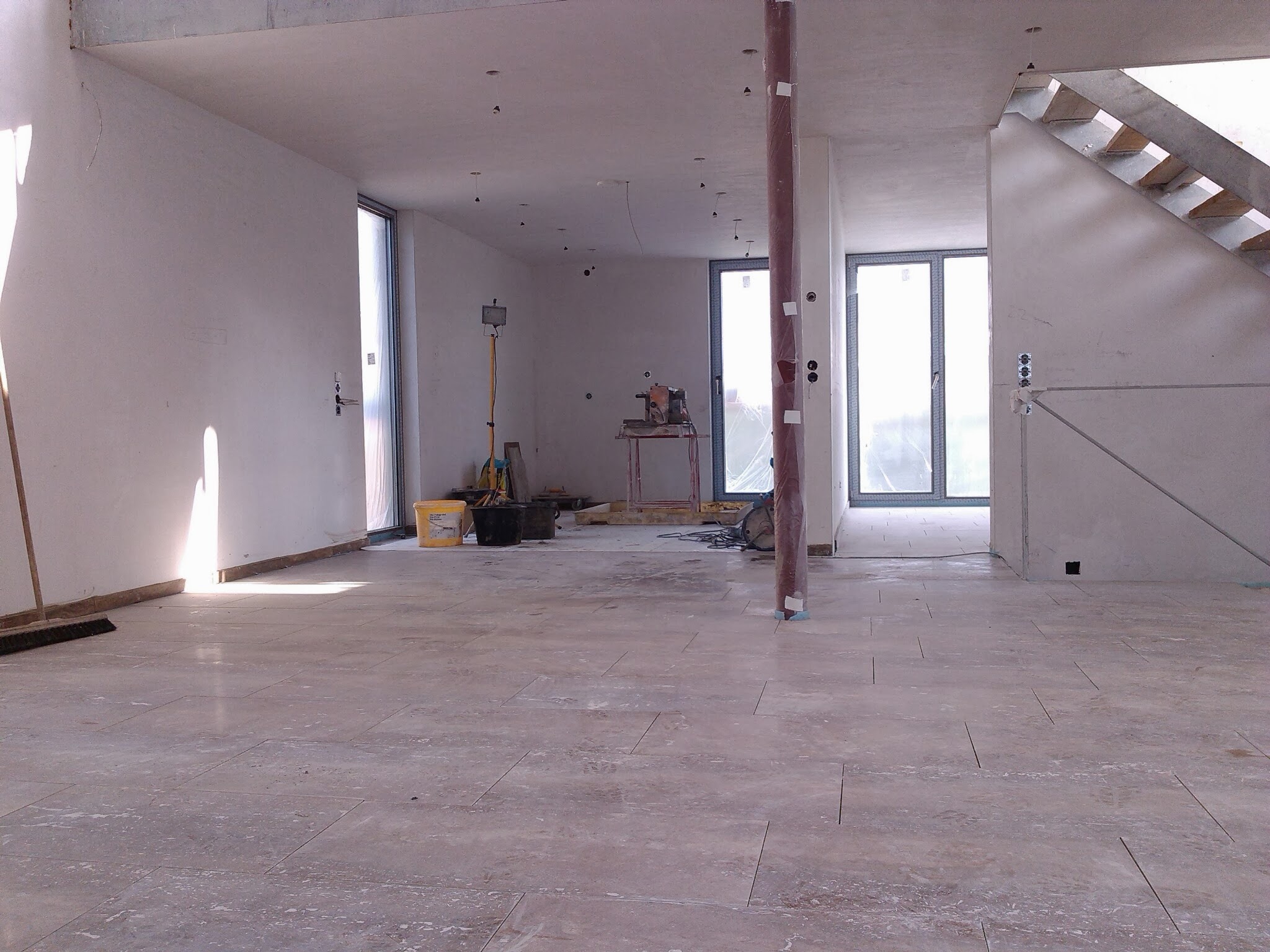 Wnętrze w trakcie remontu: położona terakota, surowe ściany, widoczne narzędzia i materiały budowlane, kolumna zabezpieczona folią.
