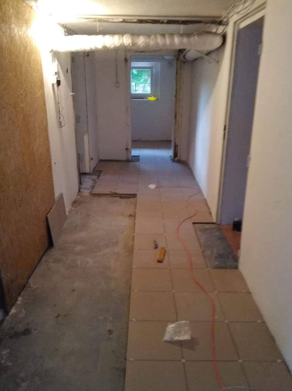 Korytarz w trakcie układania płytek podłogowych; widoczne narzędzia, kabel elektryczny i częściowo położona podłoga.