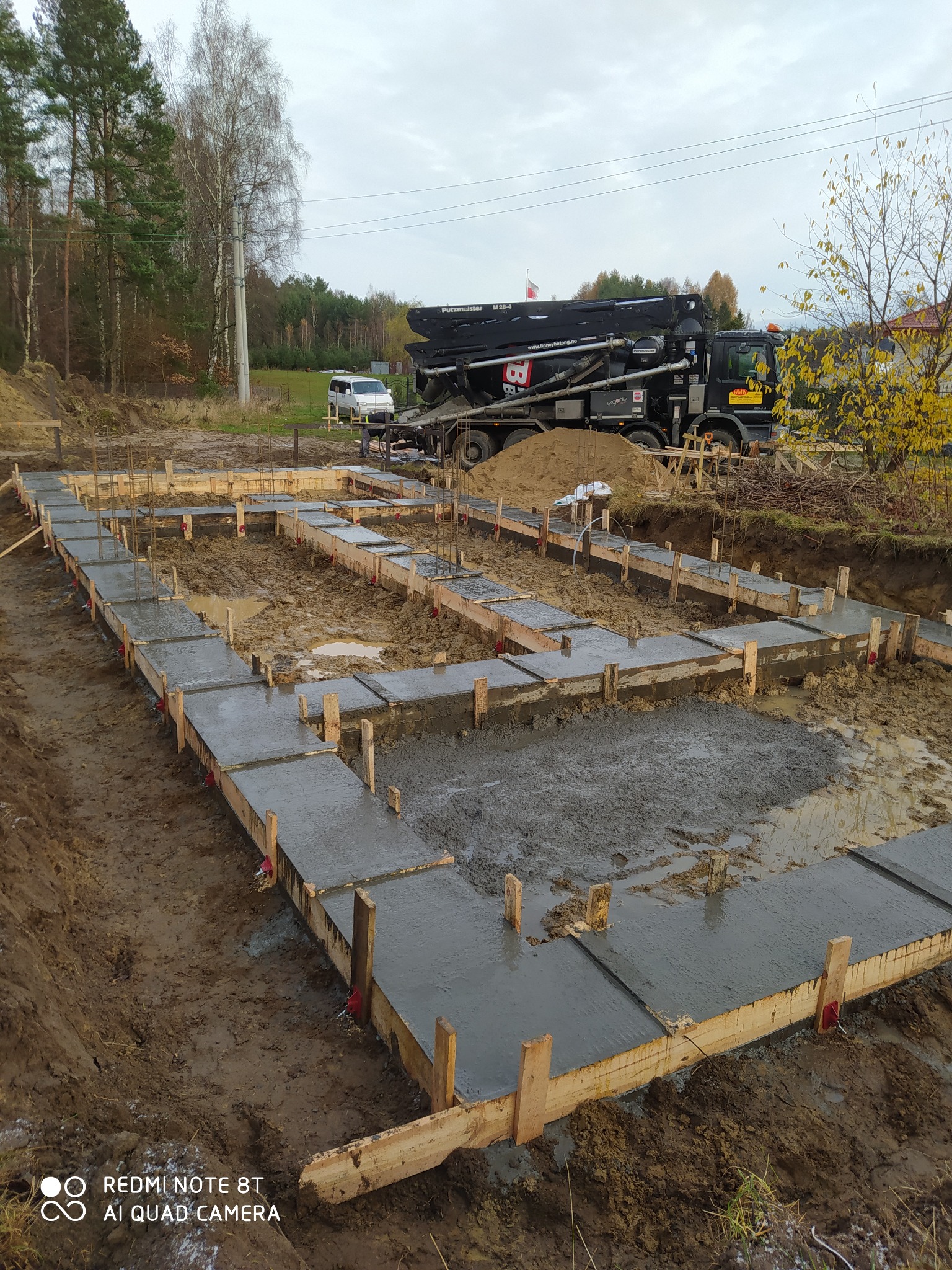 Wylane fundamenty pod dom jednorodzinny z widocznym szalunkiem i pompą do betonu na działce w pochmurny dzień.