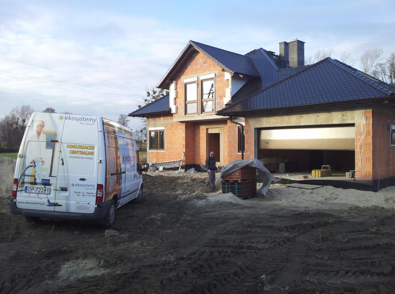 Budowa domu jednorodzinnego w trakcie montażu okien, widoczny samochód dostawczy z reklamą odkurzaczy centralnych firmy budowlanej.