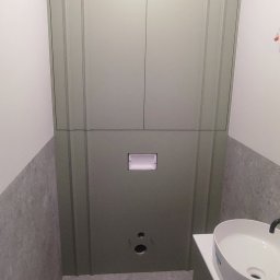 PHU PIWKO MEBLE NA WYMIAR MILENA PIWKO - Zabudowa toalety podtynkowej z szafkami w kolorze oliwkowej zieleni, umywalka nablatowa na szafce, szara płytka na podłodze i ścianach.