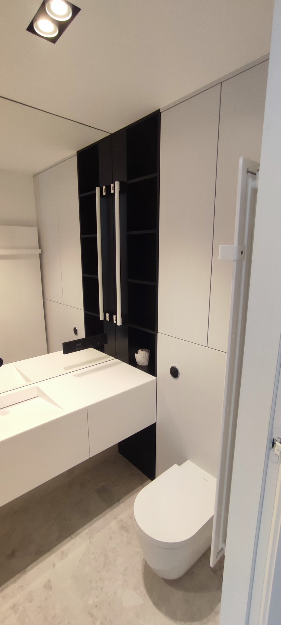 Nowoczesna łazienka z białymi szafkami na wymiar z czarnymi wstawkami, wisząca umywalka z blatem i lustrem oraz toaleta.