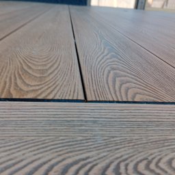 Tarasy Drewniane i Kompozytowe Arkadiusz Młynarski - Bliski kadr na deski tarasowe z widocznym usłojeniem i wąskimi szczelinami, ułożone poziomo, z perspektywą od dołu.