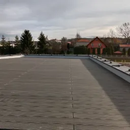 Szary taras kompozytowy na dachu budynku z widocznymi łączeniami desek i elementami wykończeniowymi, w tle zabudowa jednorodzinna.