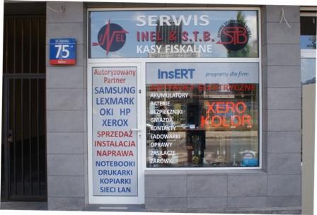 Fasada punktu serwisowego z ofertą naprawy notebooków, drukarek, kopiarek i kas fiskalnych. Na drzwiach lista autoryzowanych partnerów, w oknie neon XERO KOLOR.