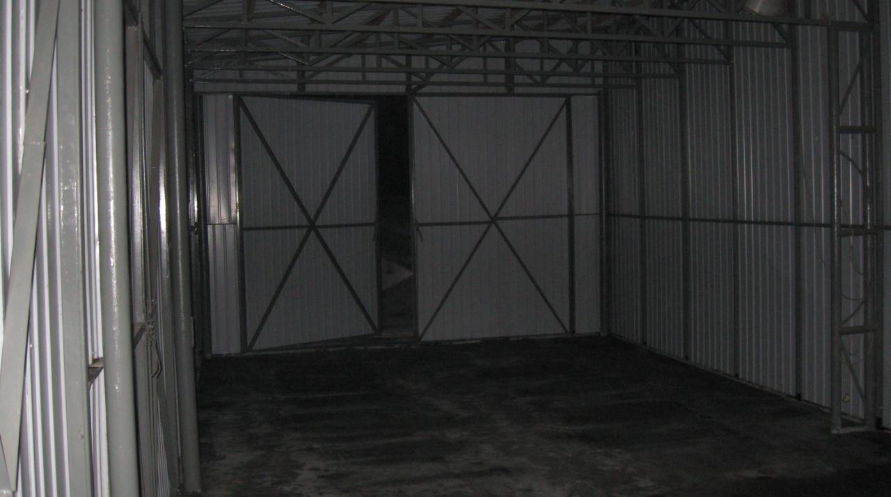 Wnętrze szkieletowego magazynu z metalową konstrukcją i częściowo otwartymi dwuskrzydłowymi drzwiami.