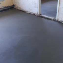 Świeżo wylana, gładka posadzka w pomieszczeniu w Babienicy, widoczne ślady po łatach na ścianach.