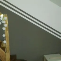 Ściana klatki schodowej pomalowana na szaro i biało z dwoma ciemnymi pasami, drewniane schody z dekoracyjnymi kulami świetlnymi.