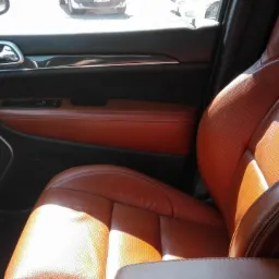 Wnętrze samochodu z brązową skórzaną tapicerką, widoczny fotel kierowcy z logo SRT, deska rozdzielcza z elementami karbonu i panel drzwiowy.