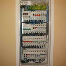 Rozdzielnica elektryczna z zainstalowanymi bezpiecznikami i przewodami w obudowie, zamontowana na ścianie wewnątrz budynku.