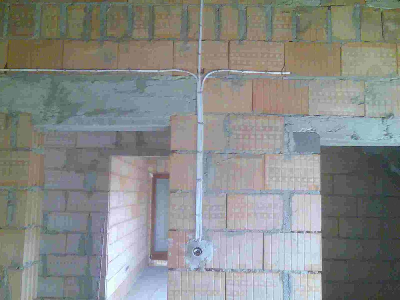 Instalacja elektryczna natynkowa w surowym stanie, białe kable rozchodzące się na ścianie z cegły, widoczne puszki instalacyjne.