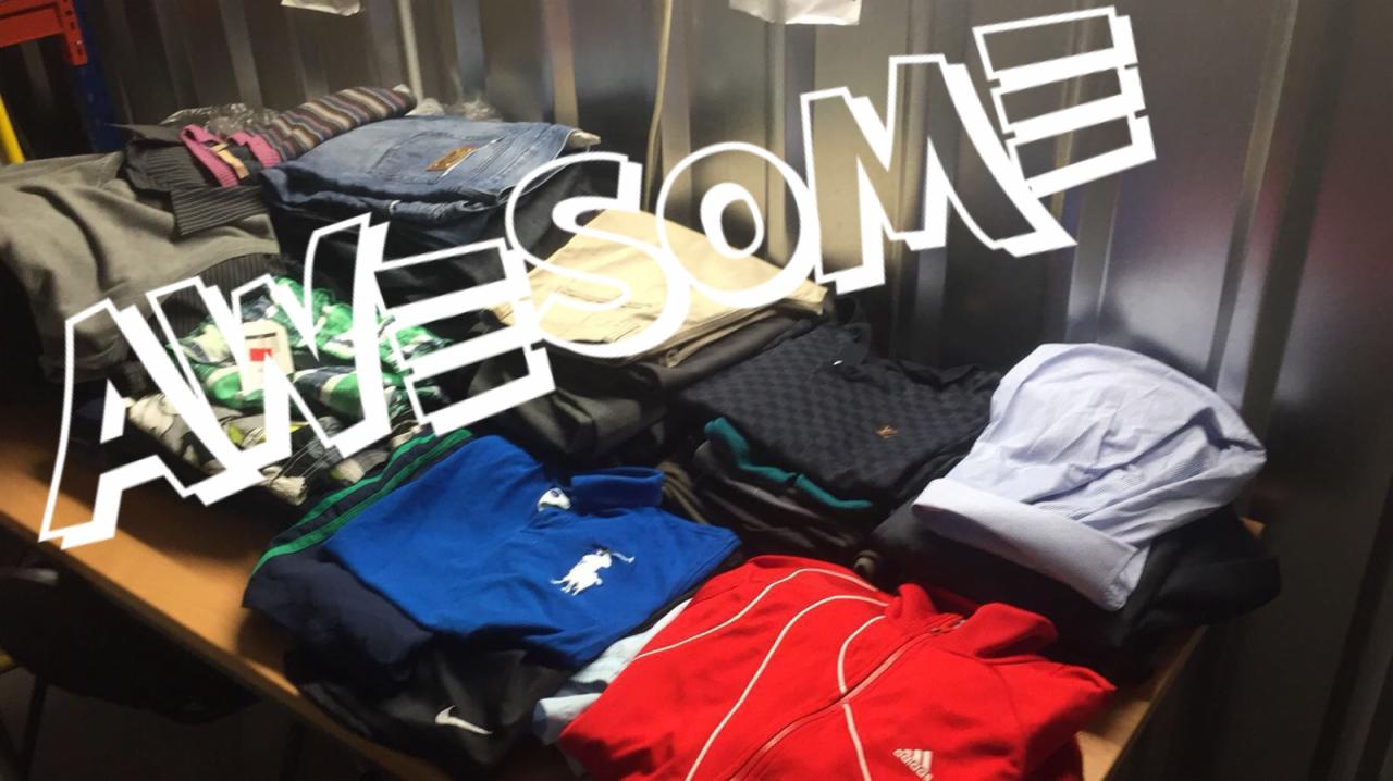 Stos ubrań różnych marek, w tym bluza Adidas i koszulka Polo, ułożonych na stole w słabo oświetlonym pomieszczeniu, z napisem 'AWESOME' nałożonym na zdjęcie.