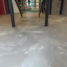 Błyszcząca, jasnoszara posadzka z efektem marmuru w pomieszczeniu z betonowymi ścianami i metalowymi elementami konstrukcyjnymi schodów.