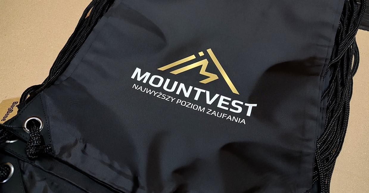 Czarne workoplecaki ze złotym logo 'Mountvest' i białym napisem 'Najwyższy poziom zaufania', widoczne sznurki i metalowe oczka.