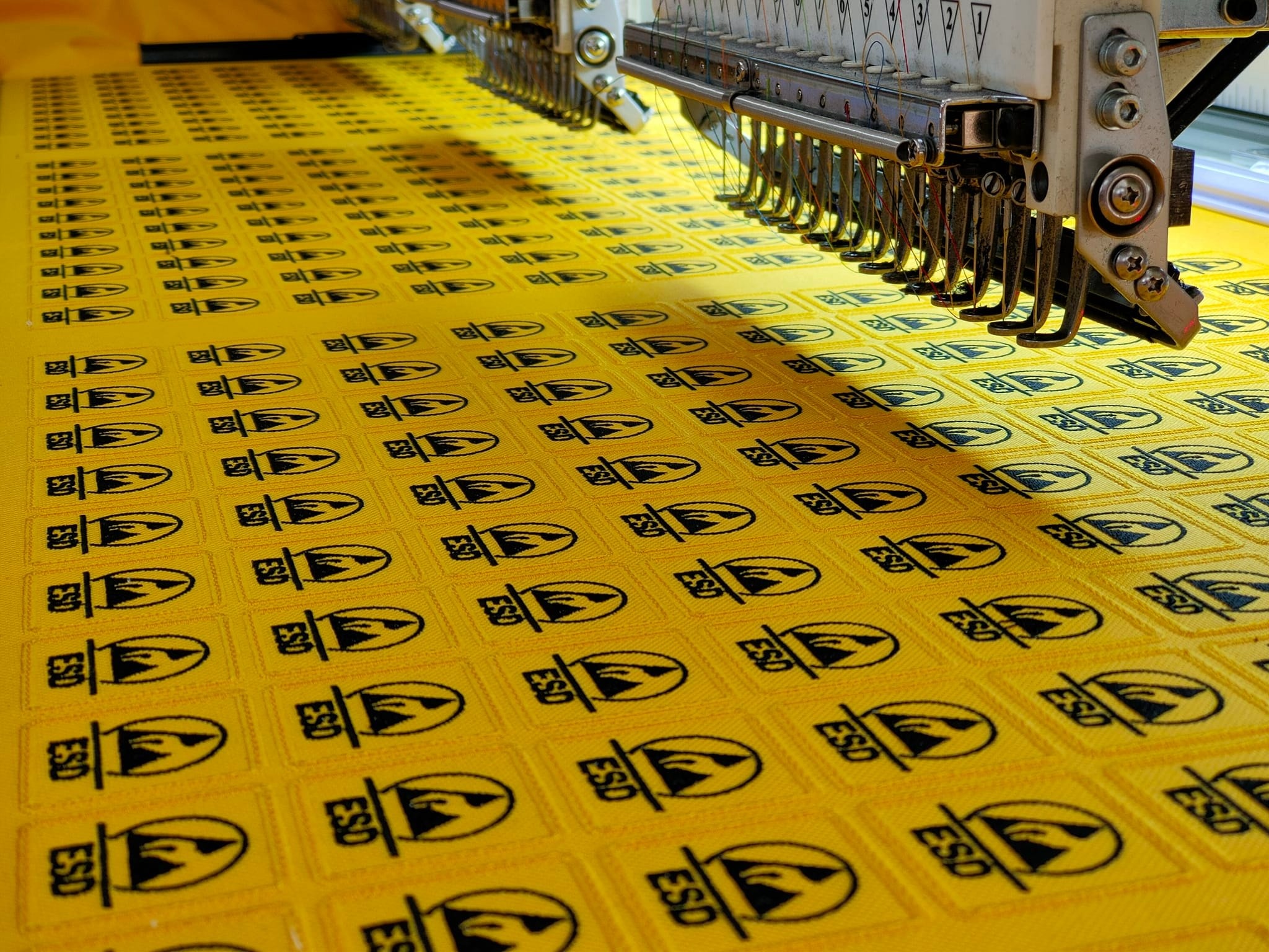 Haftowanie żółtych naszywek z symbolem ESD za pomocą przemysłowej maszyny hafciarskiej.